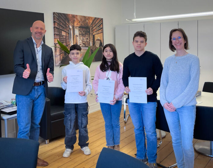 Herr Holl und Frau Grundmann stehen neben 3 Gewinner:innen der Mathe-Olympiade.