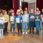 Herr Holl steht neben einigen Gewinner:innen in der Aula.