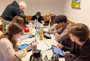 Gruppe von Jugendlichen sitzen an einem Tisch und schreiben auf ihren Ipads.