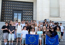 Sozialwissenschaftskurse der Q1 zu Gast in Brüssel Klassenstufe hält Europaflaggen vor Palamentshaus und lächelt