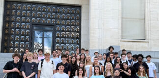 Sozialwissenschaftskurse der Q1 zu Gast in Brüssel Klassenstufe hält Europaflaggen vor Palamentshaus und lächelt