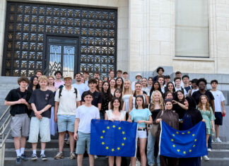 Sozialwissenschaftskurse der Q1 zu Gast in Brüssel Klassenstufe hält Europaflaggen vor Palamentshaus und lächelt