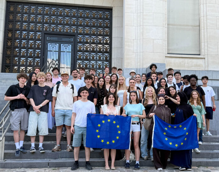 Klassenstufe hält Europaflaggen vor Palamentshaus und lächelt
